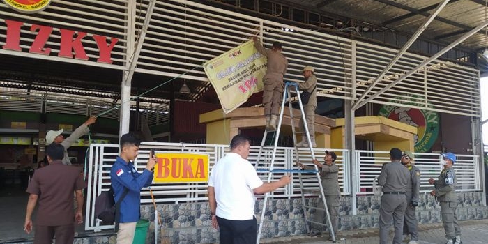Petugas Satpol PP Bangkalan saat memasang banner teguran terhadap salah satu rumah makan yang diduga tak bayar pajak secara penuh.