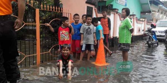 Anak-anak berjaga di depan sekolahnya yang terendam banjir luapan sungai Sadar. foto: YUDI EP/ BANGSAONLINE
