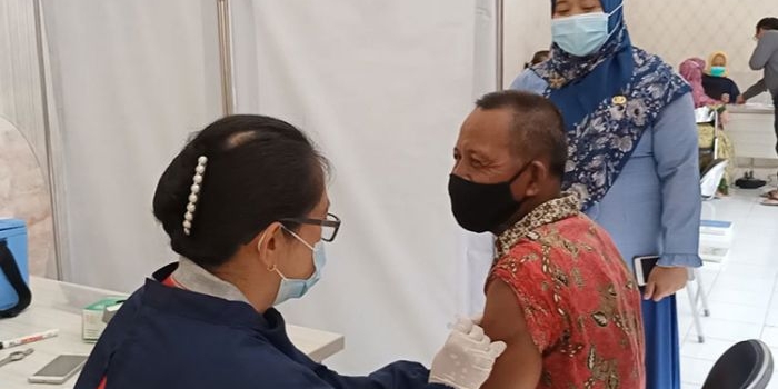 Kepala Puskesmas Pagu drg. Dewi Kasanah Murtiningsih (berdiri) saat menyaksikan pemberian Vaksin AstraZaneca kepada salah satu lansia laki-laki di Puskesmas Pagu. (foto: MUJI HARJITA/ BANGSAONLINE)