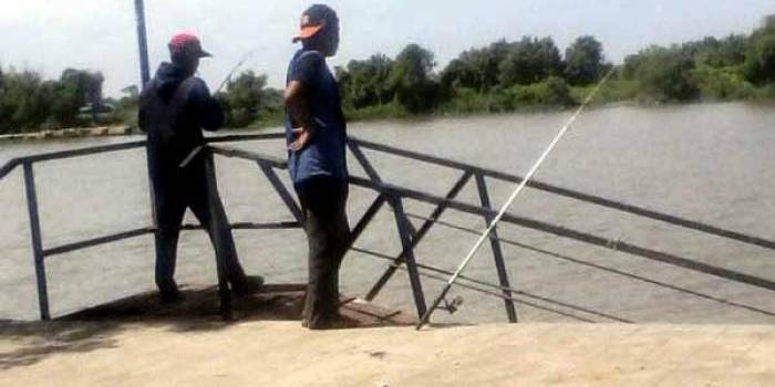 Dua penghobi mancing memanfaatkan dermaga Tlocor, dengan latar belakang pulau hutan mangrove Sarinah. foto: rizki alvian/ BANGSAONLINE