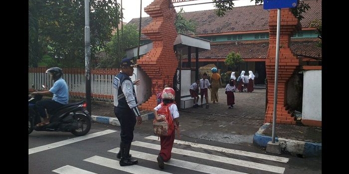 Petugas Dishub saat menyebrangkan anak sekolah.
