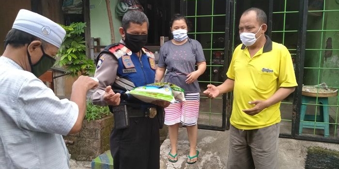 Salah satu aparat polisi sedang membagikan beras per orang 5 kg  dan uang Rp 50 ribu sedekah dari Kiai Asep Saifuddin Chalim, kepada warga Siwalankerto Utara Surabaya, Jumat (22/5/2020). foto: MMA/ BANGSAONLINE.COM