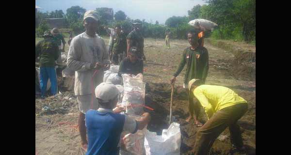 Warga dan pasukan TNI membuat tanggul buatan dari karung yang disi pasir dan kerikil.