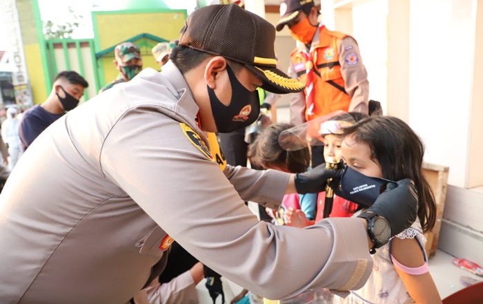Kapolres Mojokerto AKBP Dony sedang mengenakan masker kepada seorang gadis kecil.