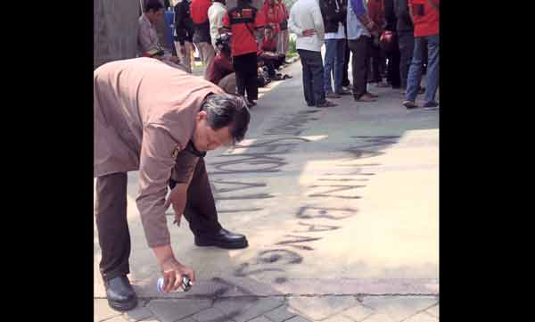 Aktivis pendidikan, Hari Susilo ketika menulis kata-kata hinaan terhadap Mahin saat demo di kantor Pemkab  Gresik. (foto: syuhud/BANGSAONLINE)