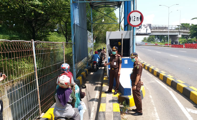 Petugas gabungan memantau penyemprotan disinfektan bagi pengendara motor di pintu masuk jembatan Suramadu, Senin (30/3).