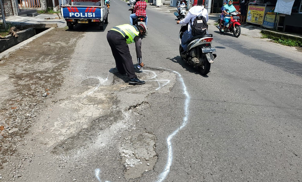 Anggota Satlantas Polres Blitar menandai jalan berlubang mengunakan cat putih.