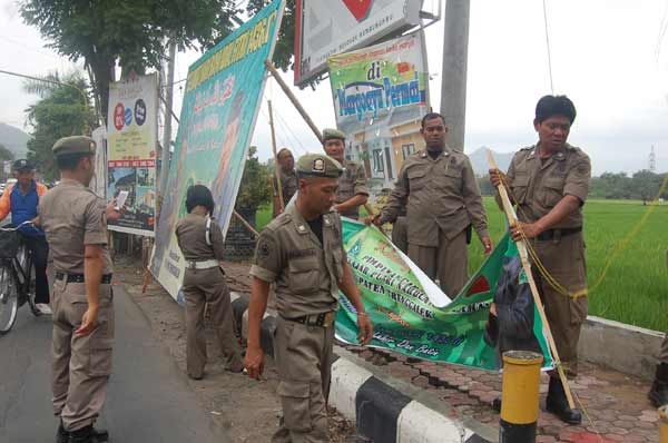 DITURUNKAN – Petugas Satpol PP Trenggalek saat menertibkan papan reklame yang melanggar aturan, di Jalan Soekarno – Hatta, Trenggalek, Kamis (30/7). foto: herman/BANGSAONLINE