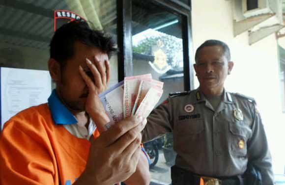 PENGECER: Tersangka Suroto Ady Wijaya menutupi wajahnya sambil menunjukkan barang bukti (BB) uang yang diterima dari menjadi pengecer togel, kemarin. foto: catur andy erlambang/BANGSAONLINE
