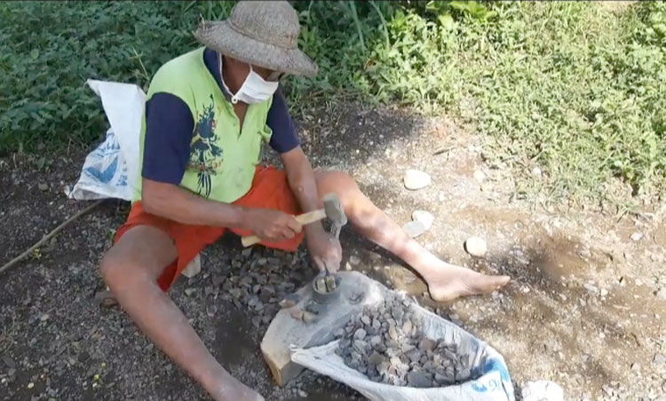 Samirin, saat memecah batu kali untuk dijadikan batu coral untuk bahan cor bangunan. (foto: MUJI HARJITA/ BANGSAONLINE)