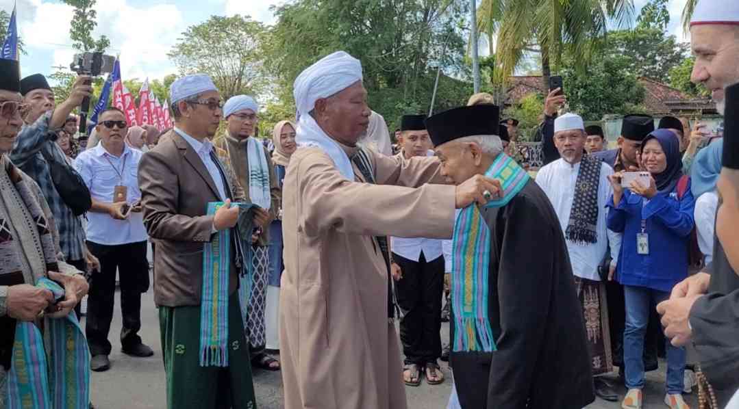 Rais Syuriah PCNU Lombok Tengah TGH Maarif Makmun mengalungkan  cinderamata kehormatan kepada Prof Dr KH Asep Saifuddin Chalim, MA, ketika menghadiri Haul Akbar TGH Lalu Muhammad Fishal Abdul Hannan di lapangan Pendopo Kabupaten Lombok Tengah NTB, Rabu (20/4/2025). Foto: MMA/bangsaonline
