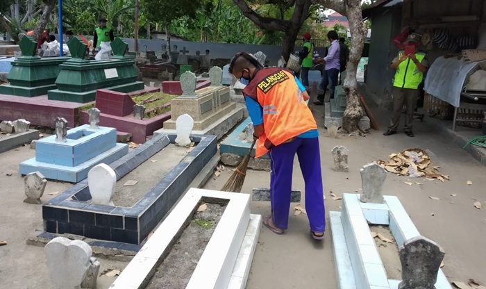 Seorang warga yang terjaring operasi yustisi mendapat sanksi membersihkan makam umum. foto: MUJI/ BANGSAONLINE
