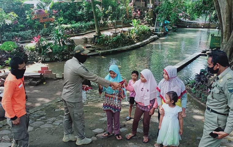 Petugas Satpol PP Kota Kediri saar membagikan masker gratis kepada pengunjung tempat wisata Sumber Banteng, sebelum mereka meninggalkan tempat. (foto: ist.)