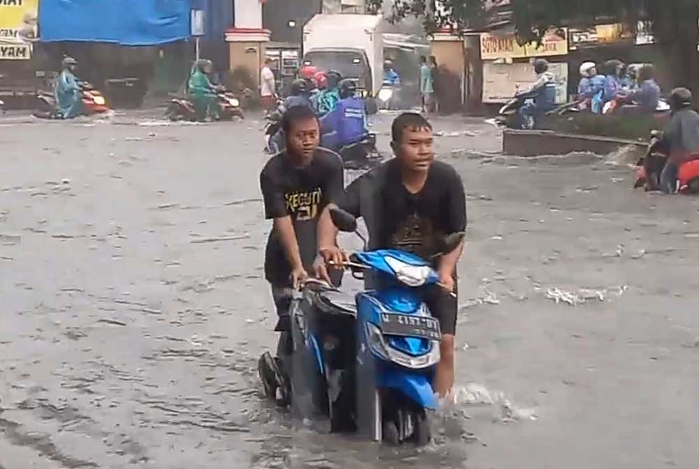 Salah satu pengendara mendorong motornya yang mogok usai nekat menerjang banjir di kawasan pintu masuk GKB. Foto: Ist.
