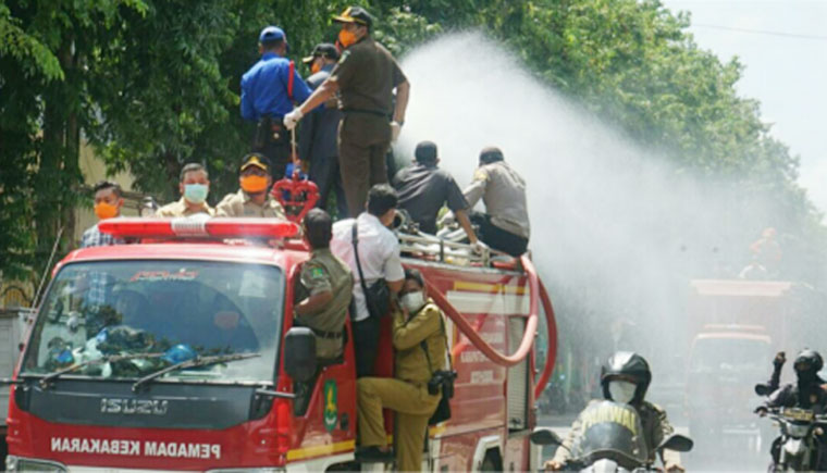 Petugas menyemprotkan disinfektan ke jalanan menggunakan mobil damkar.