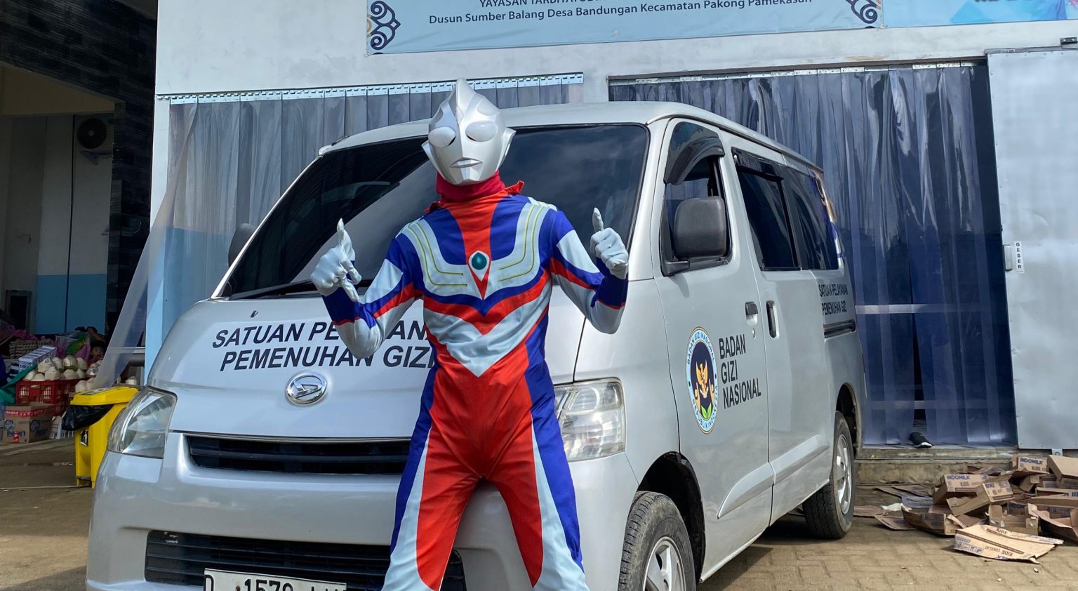 Petugas SPPG Yayasan Tarbiyatul Mubtadiin Pakong, berkostum ultraman berdiri di depan mobil SPPG